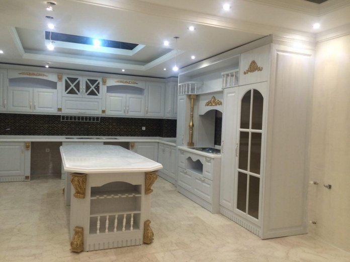 کابینت ممبران و جزیره کلاسیک سفید صدفی با منبت کاری طلایی روی کاور هود و تاج با درب ویترینی