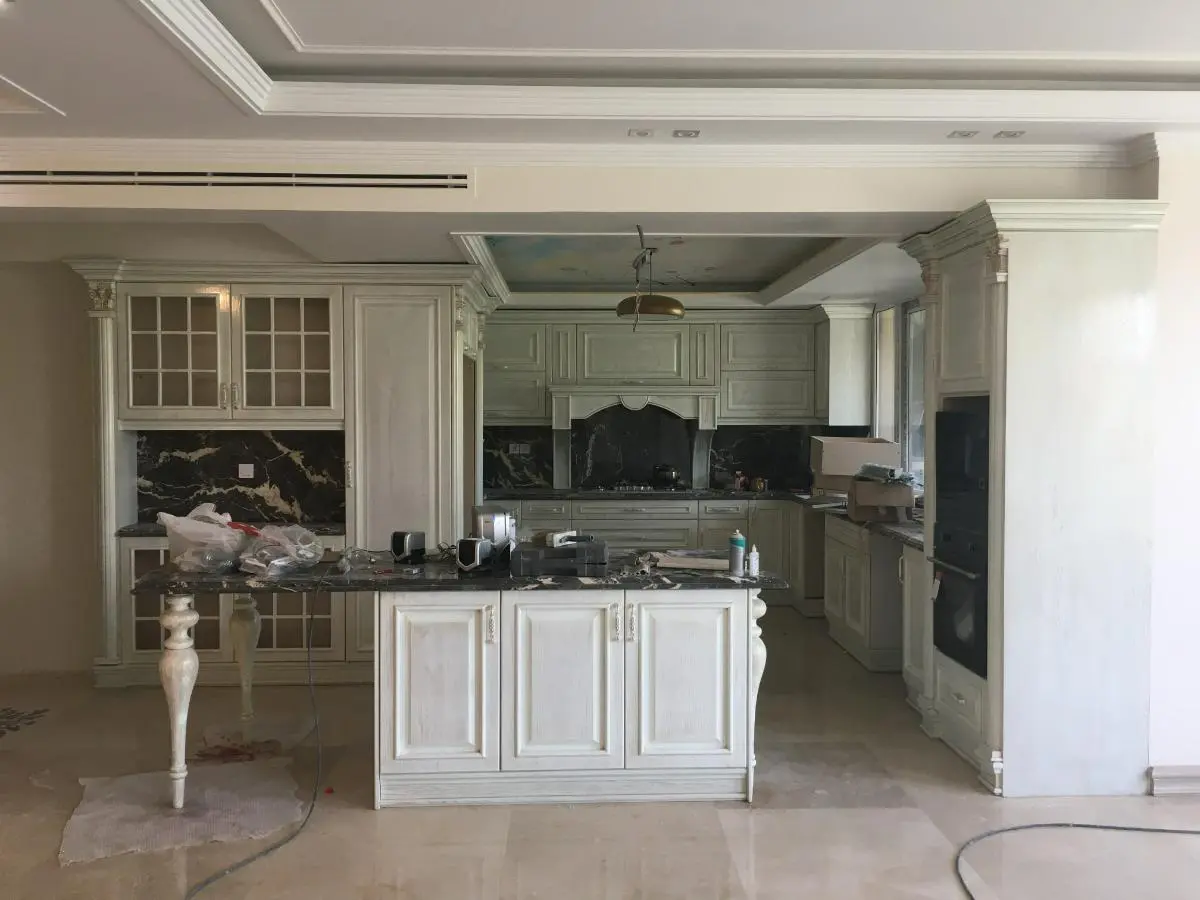 کابینت نئوکلاسیک سفید با صفحه کابینت مشکی و جزیرهای که نیمی کابینت و نیمی دیگر پایه کندهکاریشده است