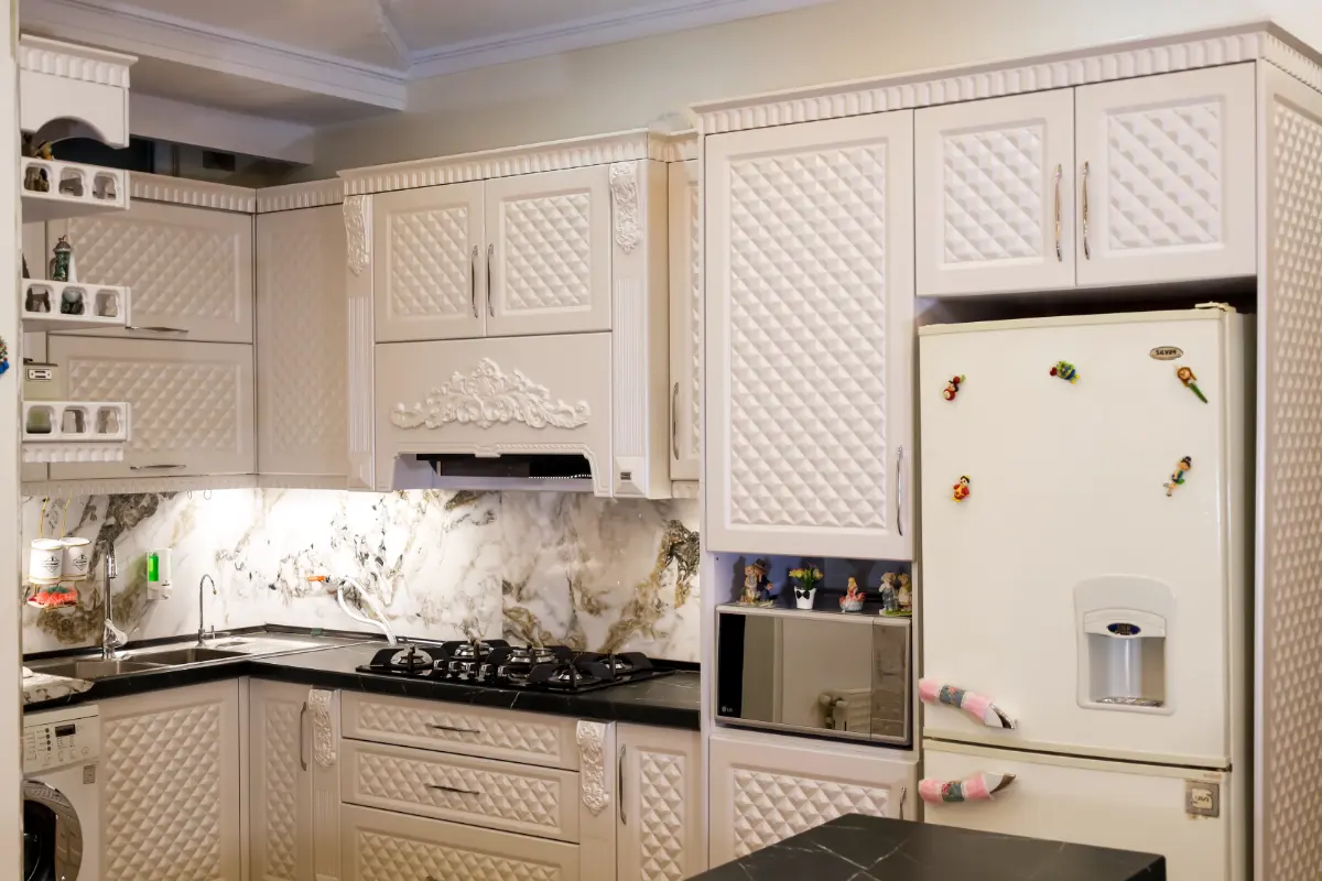 کابینت کلاسیک سفید با کندهکاریهای شلوغ وبرجسته روی درب و ستونها با دستگیره استیل ساده